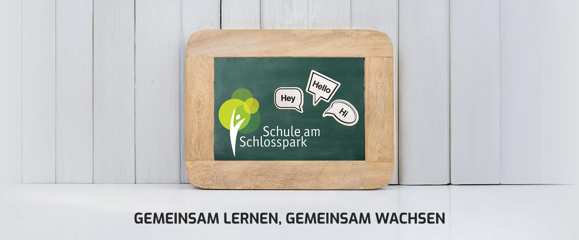 Tafel vor Holzwand mit Text: Gemeinsam lernen, gemeinsam wachsen - Schule am Schlosspark